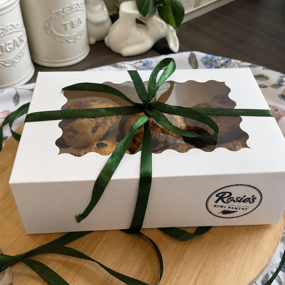 A white rectangular gift box with a window cutout, tied with a dark green ribbon, placed on a wooden board.